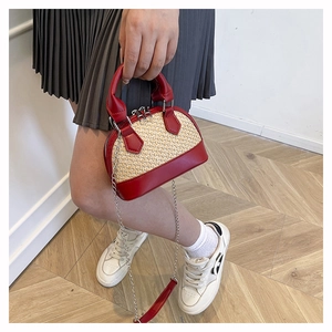 Detail of a mini red shell-shaped woven straw handbag with leather handle and chain