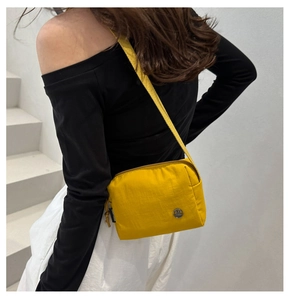 Side view of yellow nylon crossbody bag with adjustable strap on model against white stairs