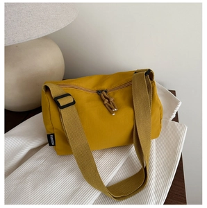 Detail of yellow nylon crossbody bag featuring adjustable wide strap and dual zippers