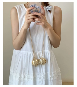 Close-up of a creative peanut-shaped gold metal bag with sparkling rhinestones and chain