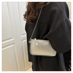 Detail of silver crocodile pattern shoulder bag featuring metallic studs and chain strap