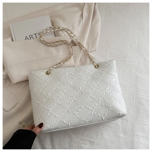 Detail of white textured tote bag with gold chain strap on minimalist cream background