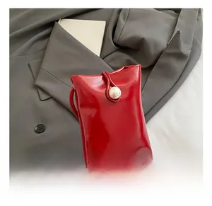 Detail of red patent leather mini crossbody bag with a decorative pearl button closure