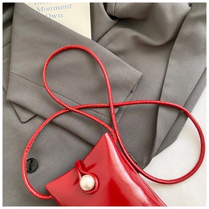 Detail of red patent leather mini crossbody bag with a large white pearl fastener