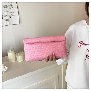 Pink woven texture clutch bag with large fold-over design held by a model in a casual setting