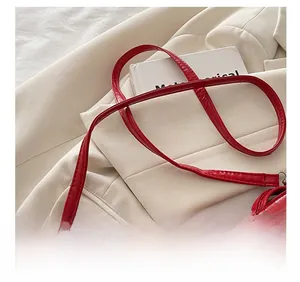 Detail of red glossy shoulder bag featuring silver buckle and adjustable strap hardware