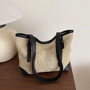 Summer woven tote bag with beige straw texture and black leather trim on a wooden table
