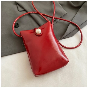 Detail of red patent leather mini phone bag with a large pearl clasp and thin strap