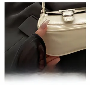 Macro shot of precise stitching and metal buckle detail on off-white leather baguette bag