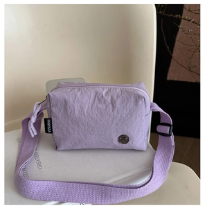 Macro detail of lavender nylon messenger bag featuring metallic logo and fabric texture