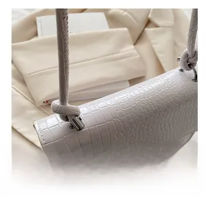 Detail of white crocodile embossed leather handbag showing the unique knotted strap design