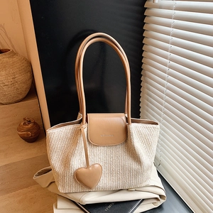 Straw woven tote bag with heart charm and leather accents in natural lighting