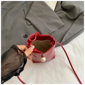 Macro view of red glossy mini crossbody bag featuring a large pearl and snap closure