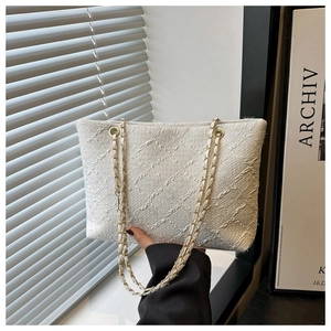 Close-up of white jacquard fabric texture and gold chain strap on a chic tote bag