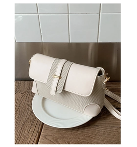 Detail of cream woven baguette bag with adjustable gold hardware on a display plate