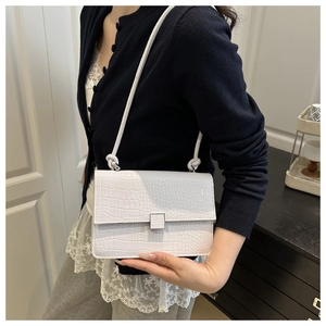Close-up of white crocodile embossed leather bag with metallic square lock and knotted strap