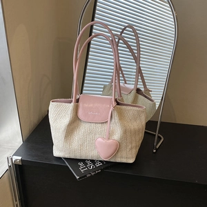 Summer woven straw tote bag with pink leather handles and heart charm in home setting