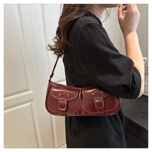 Detail view of dark red glossy underarm bag with silver buckles on a shoulder strap
