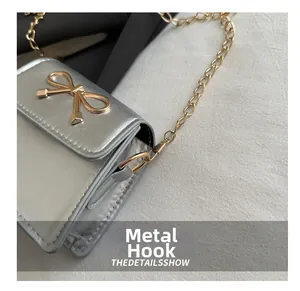 Macro view of the gold metal hook and link detail on the silver bow saddle bag