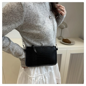 Detail of black crocodile texture bag with silver studs and chain strap on a model