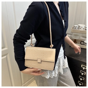 Elegant crocodile pattern flap bag in beige worn as a stylish crossbody shoulder bag