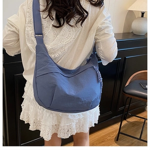 Détail du sac croissant en nylon bleu avec charme tressé et large bandoulière