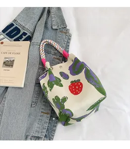 Detail of knitted bucket bag featuring red strawberry patterns and woven colorful handles
