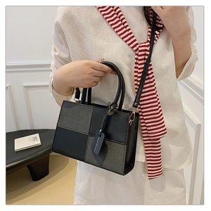 Detail of a color-block crossbody bag with grey and black patches and a fashion hangtag