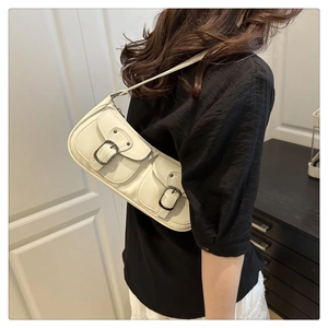 Detail of cream baguette bag featuring double front pockets and metallic buckle straps