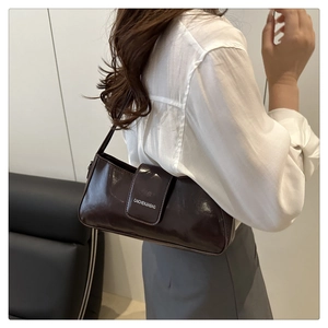 Detail of glossy chocolate brown patent leather baguette bag with minimalist white logo
