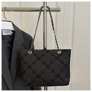 Close-up of black quilted tweed tote bag featuring gold chain strap and textured fabric