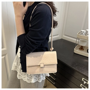 Detail of light beige croc-embossed crossbody bag with metal buckle and shoulder strap