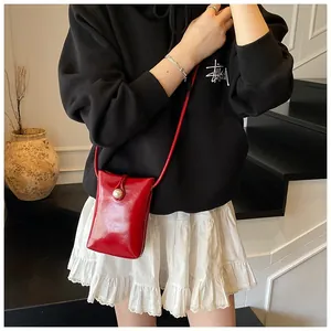 Detail of red patent leather mini phone bag featuring a large decorative white pearl