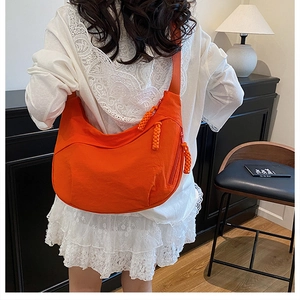 Vue détaillée d'un sac bandoulière croissant en nylon orange vif porté par un mannequin