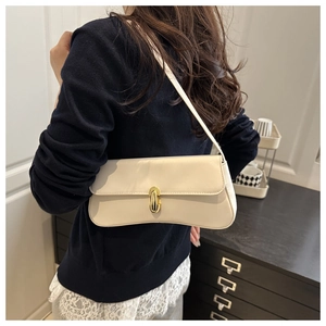 Close-up of minimalist cream baguette bag featuring a sleek golden oval buckle closure