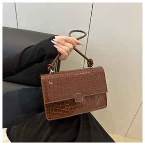 Detail view of dark brown croc-textured handbag with a silver square clasp and knotted strap