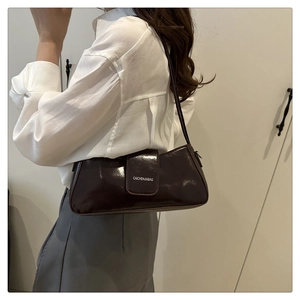 Close-up of dark brown patent leather baguette bag with shiny mirror finish and logo print