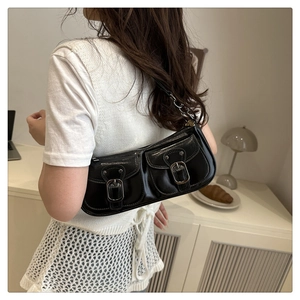Detail of a black patent leather shoulder bag with dual pockets and silver metal buckles