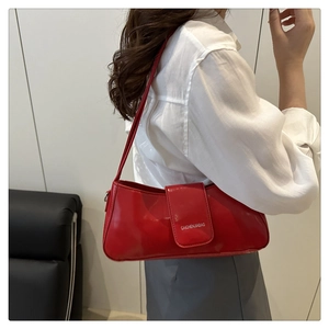 Red glossy patent leather shoulder bag detail shown on model in a minimalist setting