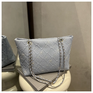 Detail of light blue tote bag featuring white floral embroidery and gold chain strap