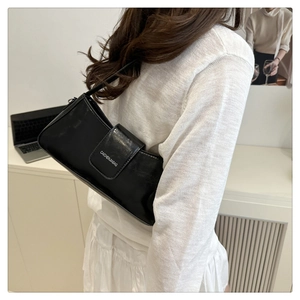 Detailed view of black patent leather shoulder bag worn by model in a minimalist setting