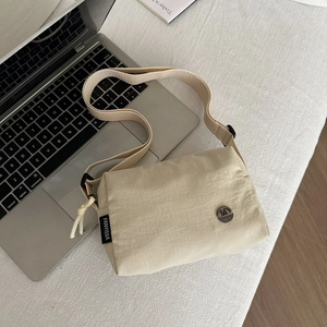 Beige pleated nylon crossbody bag with wide strap displayed on a laptop