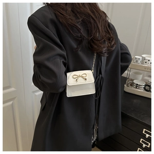 Detailed view of a white mini bow saddle bag with gold chain strap on black blazer