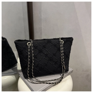 Detail of black quilted tote bag with gold chain strap and shimmering lattice texture