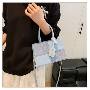 Detail of light blue and grey patchwork crossbody bag with decorative fashion tag