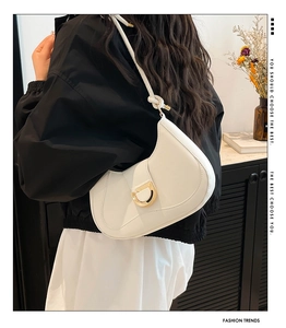 Detail of white leather crescent bag featuring a prominent gold D-buckle and knotted strap