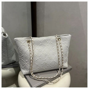 Close-up of quilted white tote bag with golden chain straps and woven texture details