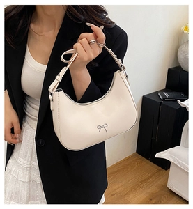Detail of a creamy white crescent bag with a silver metal bow and zipper closure