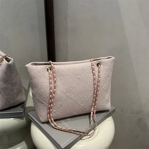Pink checkered quilted tote bag with gold chain strap placed on a white stool decor