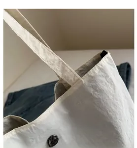 Detail showing smooth stitching on the strap and metallic logo on beige tote bag